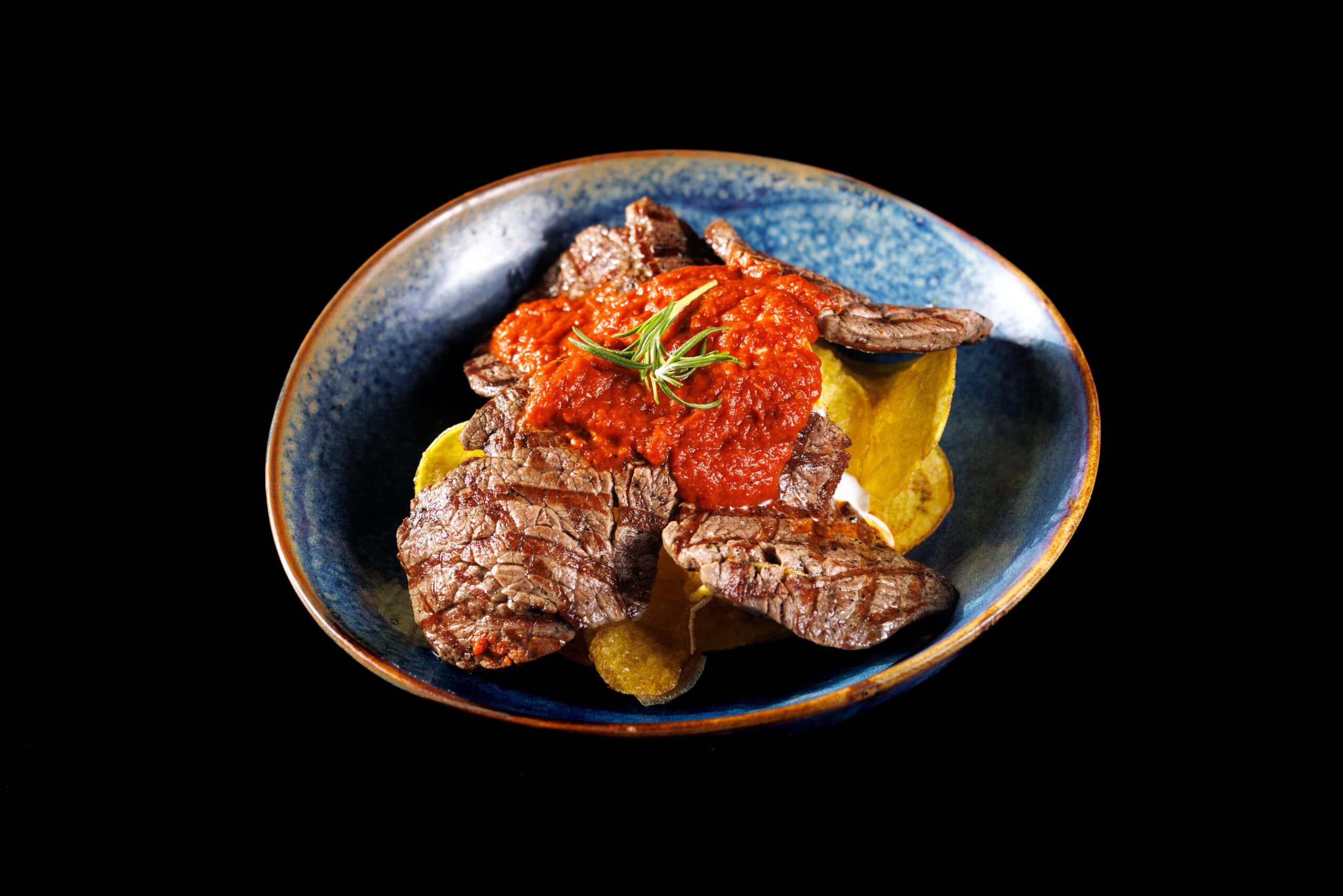 Grilled meat with tomato sauce on a blue plate
