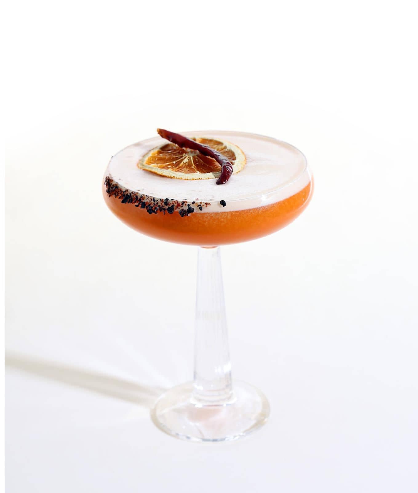 Orange cocktail in a coupe glass with dried fruit garnish
