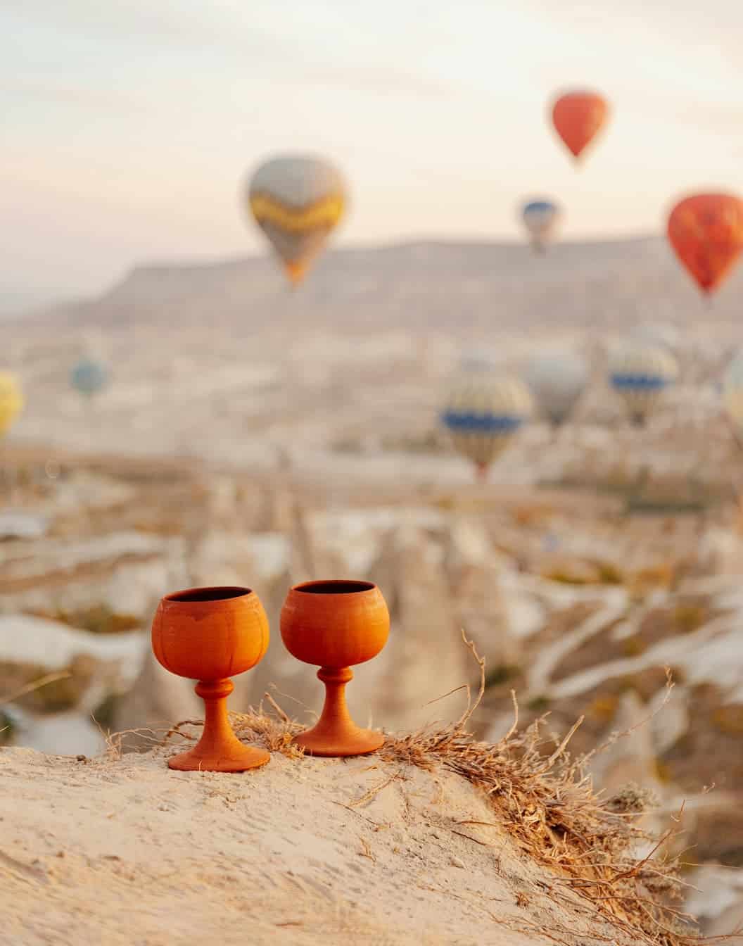 Two wine glasses on a rock with hot air balloons in the background