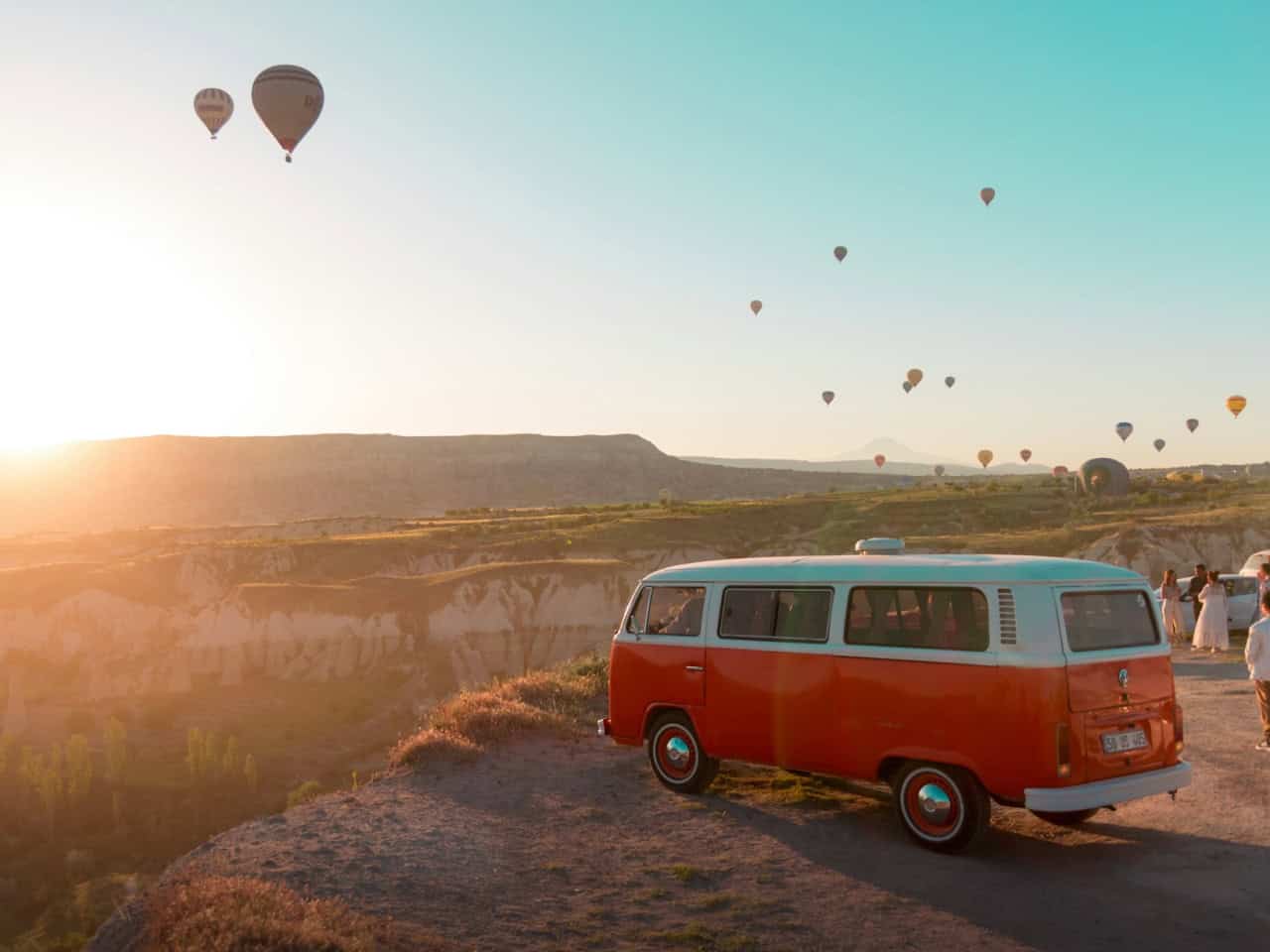 Vintage van on a hilltop with hot air balloons at sunrise in Cappadocia
